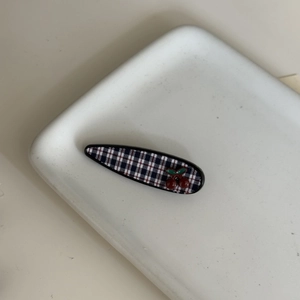 Detail of navy plaid hair clip featuring 3D red cherry accents on white ceramic plate