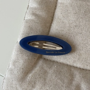 Barrette ovale rétro en acétate bleu foncé avec lettrage doré sur fond textile beige clair
