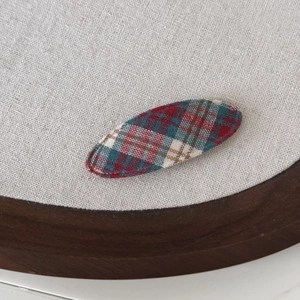 Classic blue and red plaid fabric BB hair clip with textured weave on a minimalist board