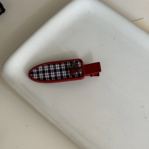 Close-up of red plaid cherry hair clip on a white ceramic plate with metal duckbill base