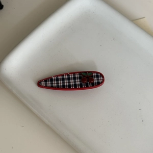 Red plaid hair clip with 3D cherry decoration on white tray 45-degree view