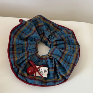 Detail of red and blue plaid fabric scrunchie with a white tag and small red bow decoration