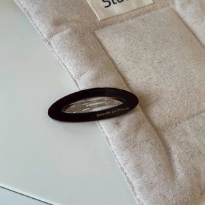 Détail macro de la barrette ovale en acétate avec élégant lettrage doré sur tissu