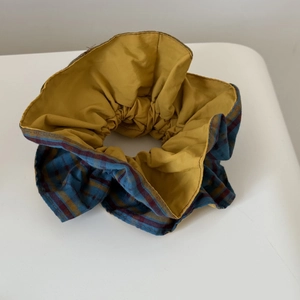 Close-up of a blue and red plaid fabric scrunchie with mustard yellow inner lining layer