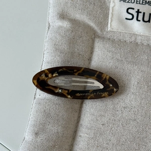 Détail macro d'une barrette ovale en acétate avec motif écaille sur pochette en lin