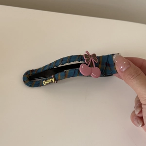 Detail of blue plaid fabric hair clip with pink cherry ornament and yellow lettering