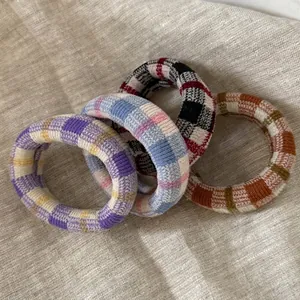 Four colorful knit plaid hair scrunchies on beige linen for high elasticity and comfort