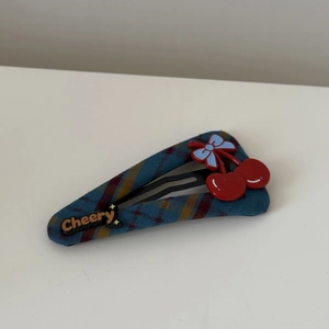 Detail of red cherry and blue bow decoration on a plaid fabric hair clip for women
