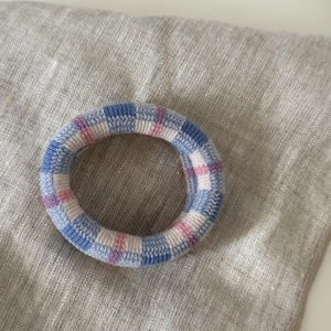 Blue and pink plaid knit elastic hair tie placed on a textured grey linen fabric background