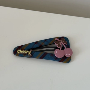 Close-up of blue plaid fabric hair clip with pink cherry and Cheery text detail
