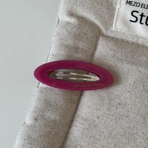 Détail de la pince à cheveux ovale rose avec lettrage doré sur tissu matelassé