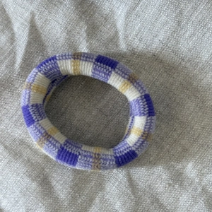 Detail shot of purple and yellow checkered knit hair tie on linen fabric background
