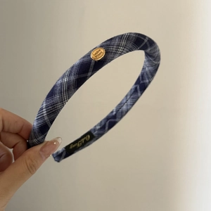 Detail of blue plaid headband with a round gold smile emblem and soft fabric texture