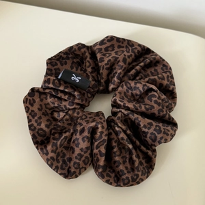 Close-up of brown leopard print velvet scrunchie with a black woven logo tag