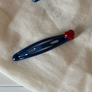 Dark blue metal hair clip with glossy red heart decoration on beige linen background