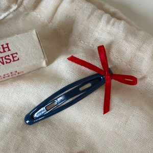 Close-up of a navy blue metal snap clip featuring a narrow red ribbon bow hair accessory