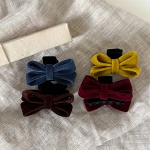 Detail view of four velvet bow hair clips in navy, mustard, brown, and wine red colors