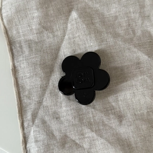 Detail of a shiny black acetate flower hair clip with wer wer text on linen background