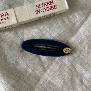 Detail of dark blue velvet BB hair clip with gold Smile Happy metallic emblem on linen