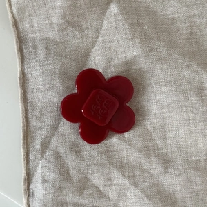 Detailed close-up of a red acetate flower hair clip with central letter engraving detail