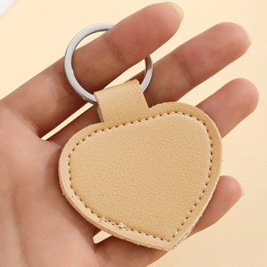 Close-up of heart-shaped beige PU leather keychain held in hand showing stitch details