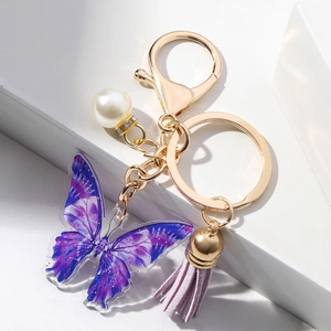 Acrylic butterfly keychain with purple suede tassel and pearl on a white geometric stage