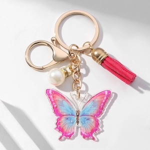 Macro detail of gradient pink blue butterfly keychain with red tassel and pearl accent