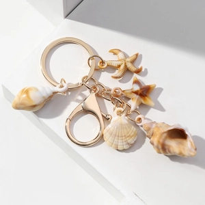 Detail of seashell keychain with golden metal ring and starfish pendants on white surface