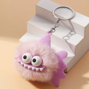 Pink furry monster keychain with purple silicone hat and silver metal ring on white stand