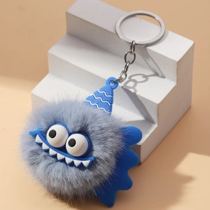 Close-up of a blue plush monster keychain with big eyes on a white geometric stand