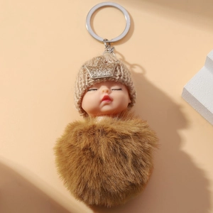 Cute sleeping baby plush keychain with brown knit hat, gold crown and fluffy fur pom-pom