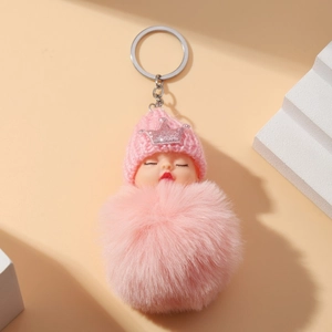 Pink plush sleeping doll keychain with knitted hat and sparkling crown on warm background