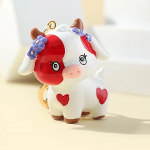 Close-up of 3D cartoon cow keychain with red heart pattern and golden metal ring
