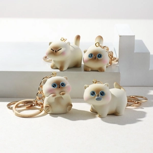 Detail view of four 3D resin cartoon cat keychains with gold metal rings on white pedestals