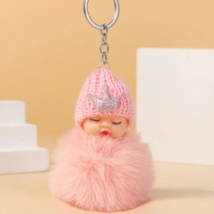 Close-up of sleeping baby doll keychain with pink knit hat, crown and plush pompom
