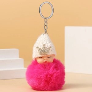 Close-up of cute sleeping doll keychain with pink fur pompom and golden crown on a white hat
