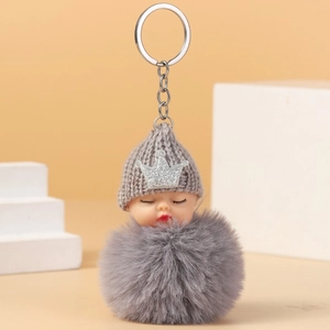 Close-up of sleeping baby doll keychain with a grey knit hat and fluffy faux fur pompom