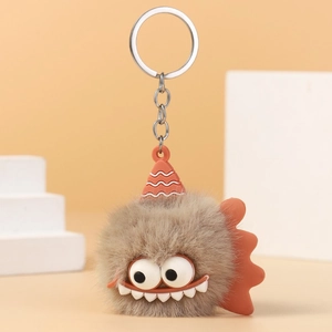 Detailed view of furry monster keychain with orange hat and sharp white teeth