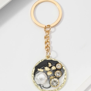 Dettaglio portachiavi dorato con disco in resina bianco e nero, strass e perla elegante