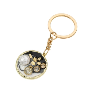 Elegante portachiavi dorato con disco smaltato bianco e nero, perle intarsiate e cristalli