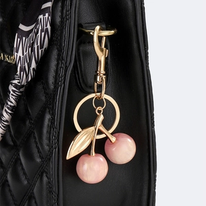 Detail of pink pearl cherry charm with gold metal leaf on a black leather handbag
