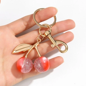 Close-up of glittery red resin cherry keychain with golden metal ring held by hand