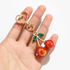 Cute cherry keychain with red resin fruit and gold heart clasp held in hand