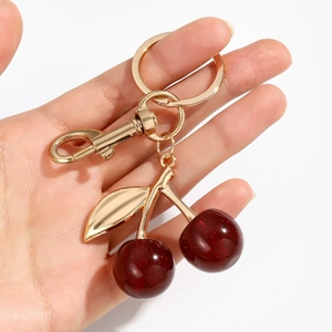Sparkly red resin cherry keychain with golden leaves and lobster clasp on white background