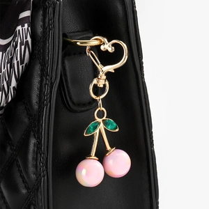 Close-up of pink iridescent cherry charm with green crystals on a black quilted bag