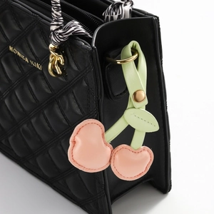 Detail of pink cherry pendant and striped scarf on quilted black leather bag