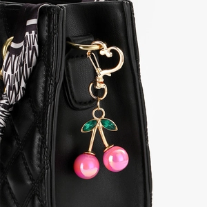 Pink pearlescent cherry keychain with golden heart clasp on a black quilted bag