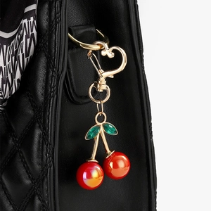 Macro view of colorful cherry keychain with heart hook on black quilted leather bag