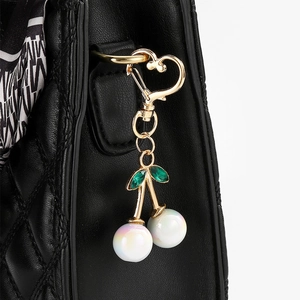 Detail of cherry keychain with golden heart clasp and green gems on a black bag