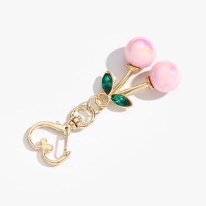 Detail of pink iridescent cherry keychain with green gem leaves and golden heart clasp